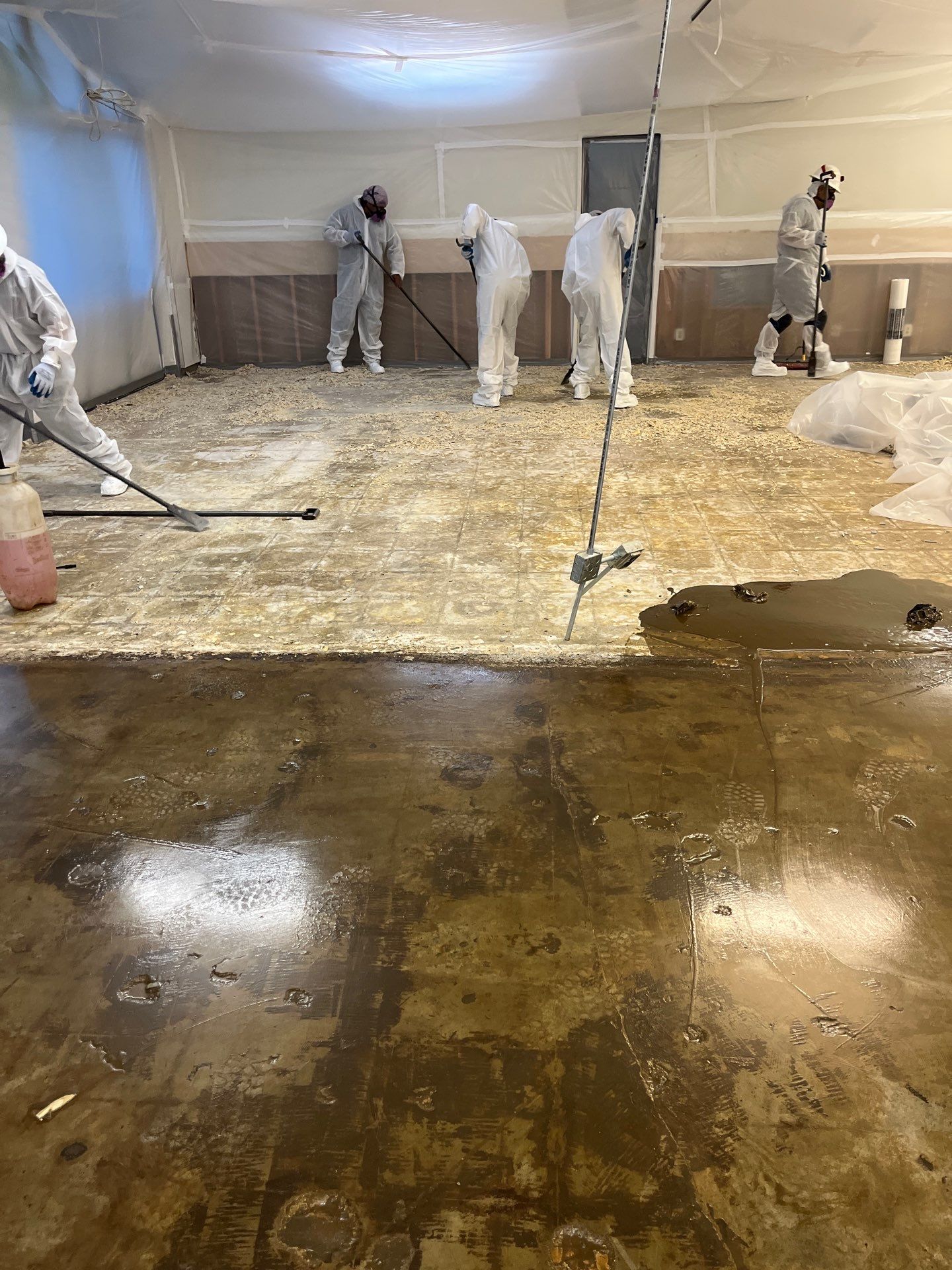 Workers removing flooring inside a plastic containment area